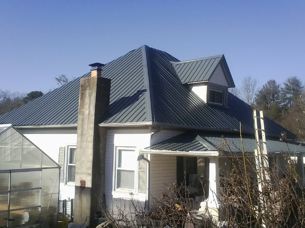 Dark blue standing seam metal roof on a white farmhouse with dormer — Slate & Tile Roof Repair by Roofing Brothers in Luzerne