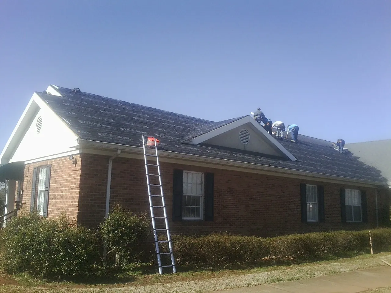 Crew tearing shingles off a brick ranch roof with a ladder set — Emergency Roof Repair work by our crew in Luzerne