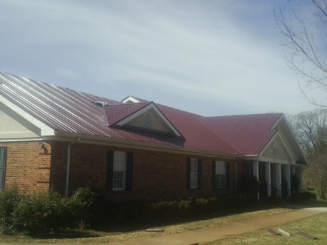 Red metal roof with gabled entries on a long brick building, from a Hail Damage Roof Repair job in Luzerne
