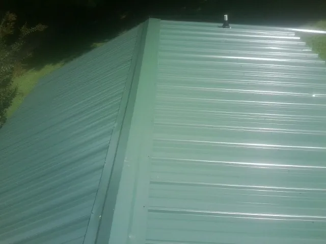 New green metal panels meeting at the ridge of a roof — Flat Roof Repair work by our crew in Luzerne