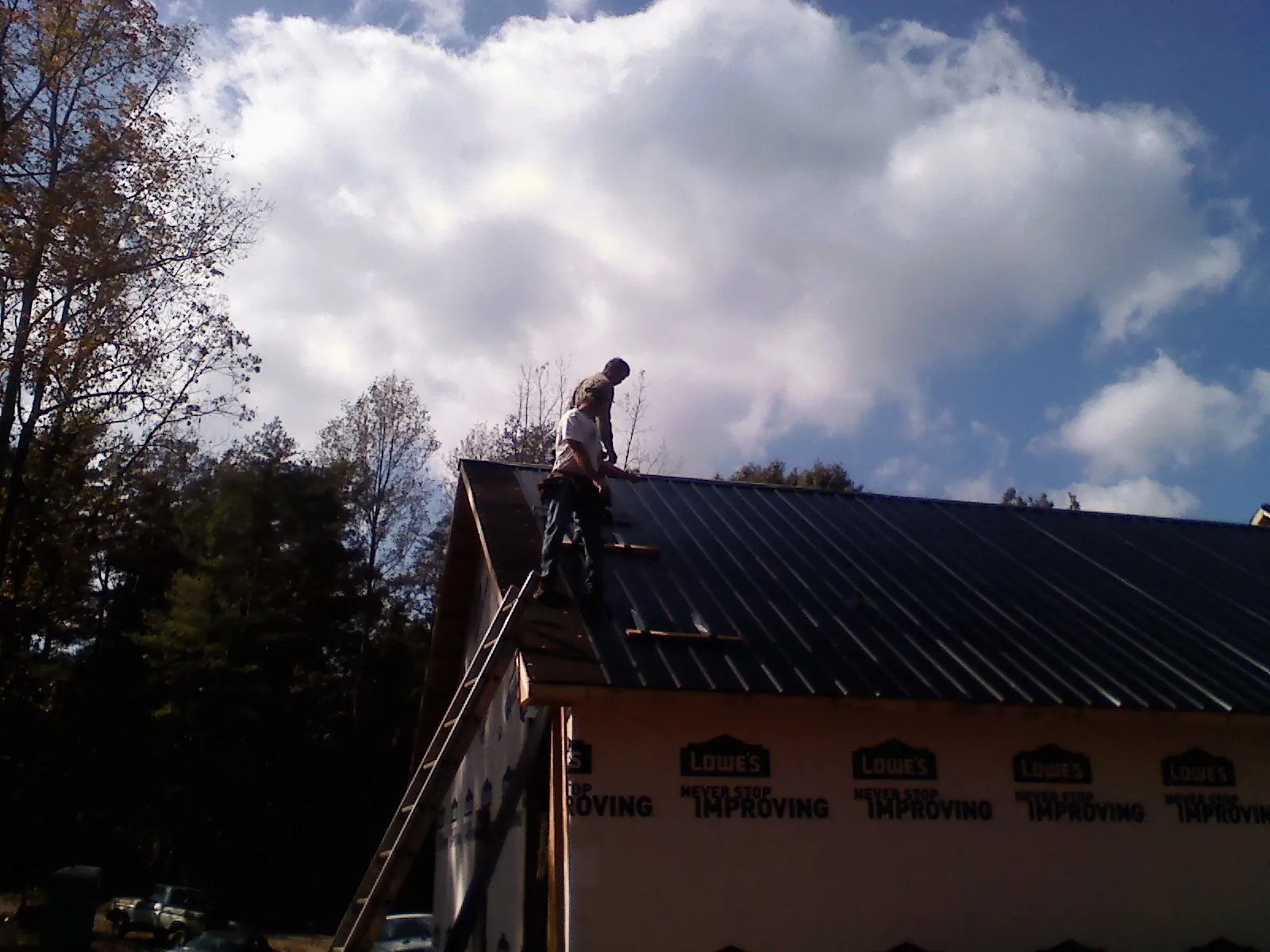 Roofer fastening dark metal panels high against a cloudy sky, from a Roof Inspection job in Luzerne