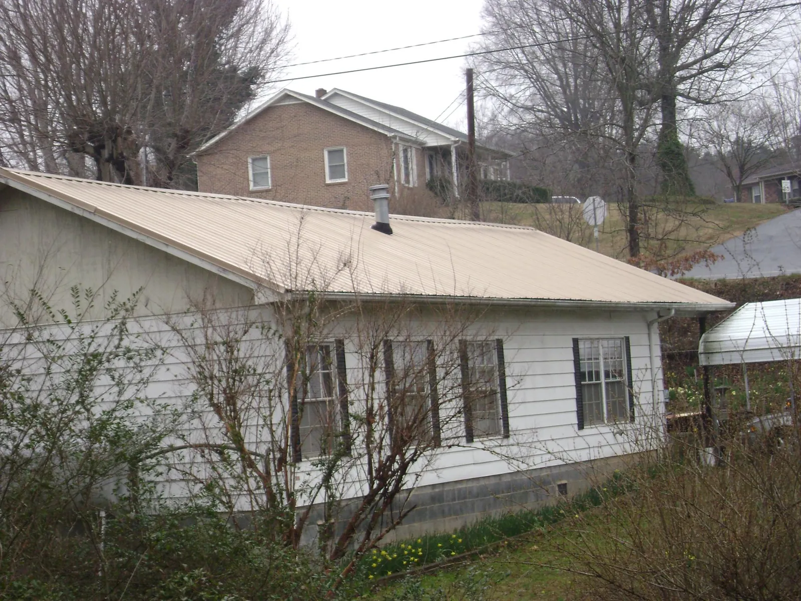 Tan metal roof on a white sided house set into a hillside — Commercial Roofing by Roofing Brothers in Luzerne